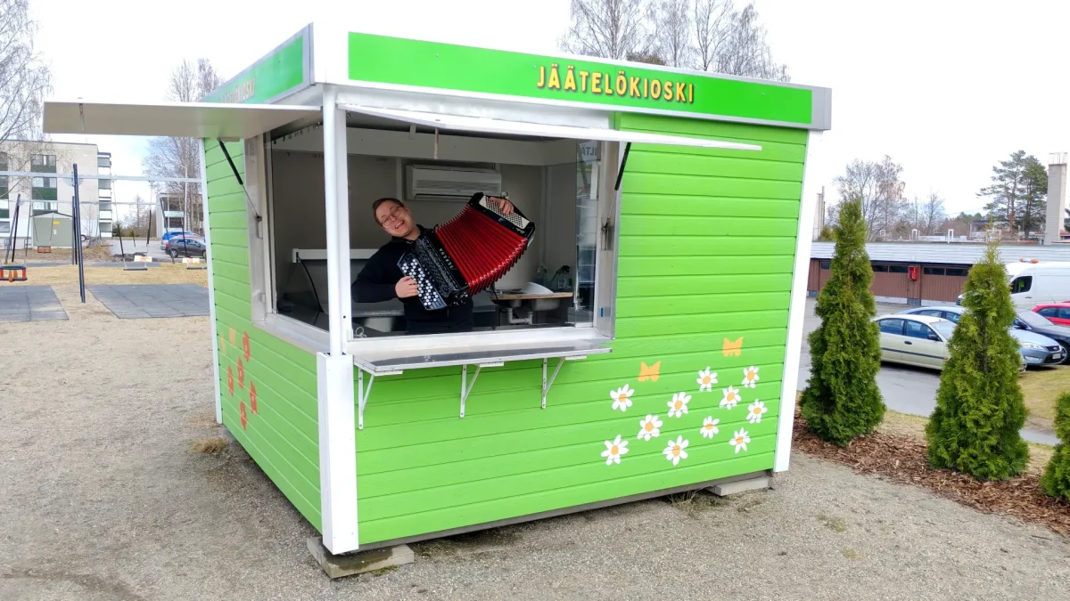 kuvassa vihreä jäätelökioski, jonka sisällö on miesoletettu soittamassa haitaria.