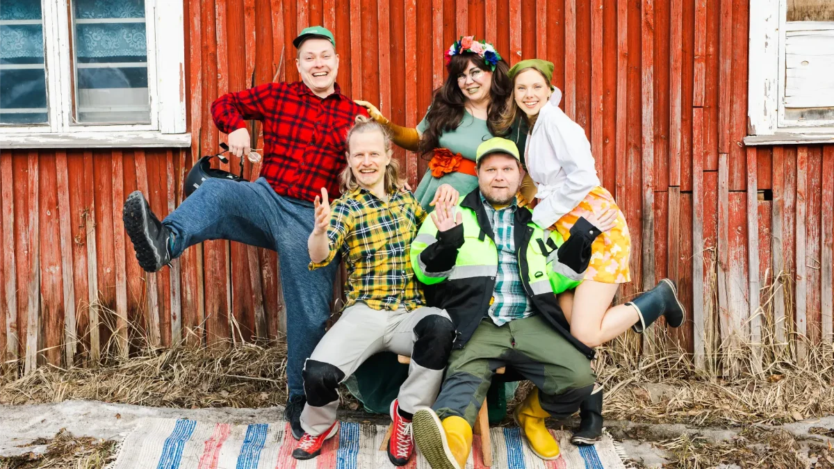 iloinen ja värikäs teatteriryhmä, viisi henkilöä punaista seinää vasten.